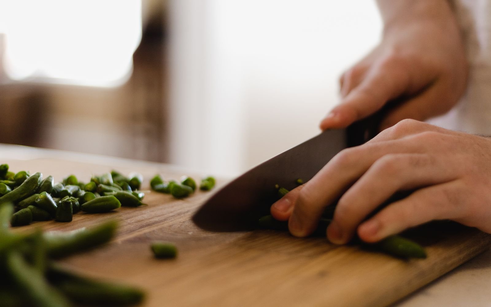 Mains coupant des haricots verts frais sur une planche