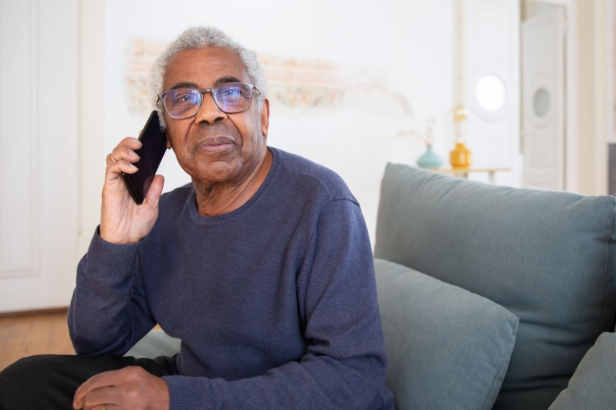 Un homme retraité téléphone depuis son canapé, un dossier posé à côté de lui